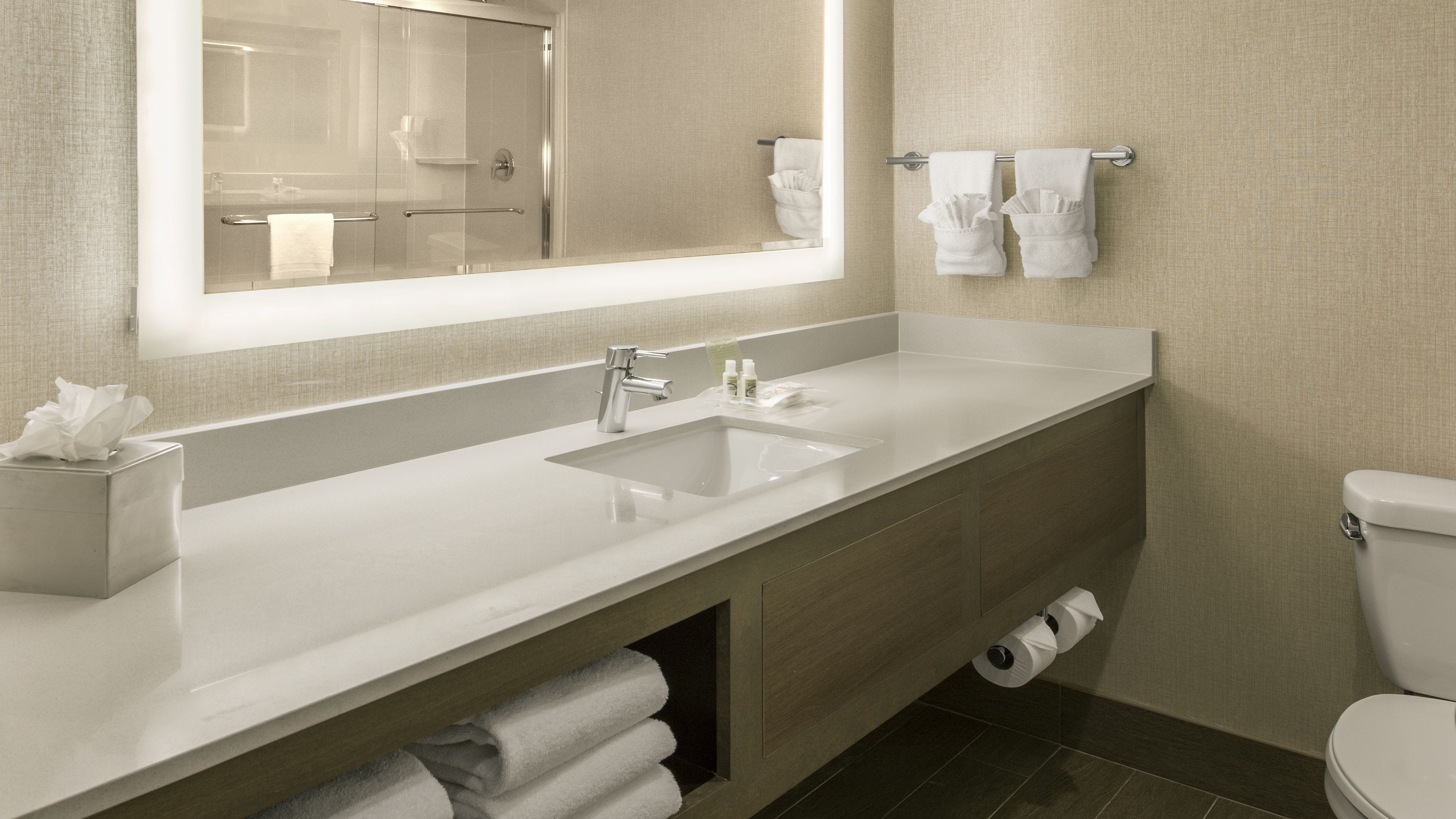 A modern bathroom with a large mirror, a white sink, a toilet, and a towel rack.