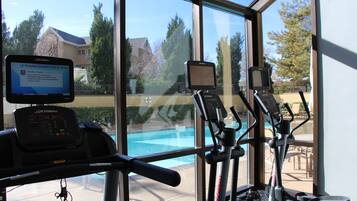A gym with exercise equipment and a large window overlooking a swimming pool.