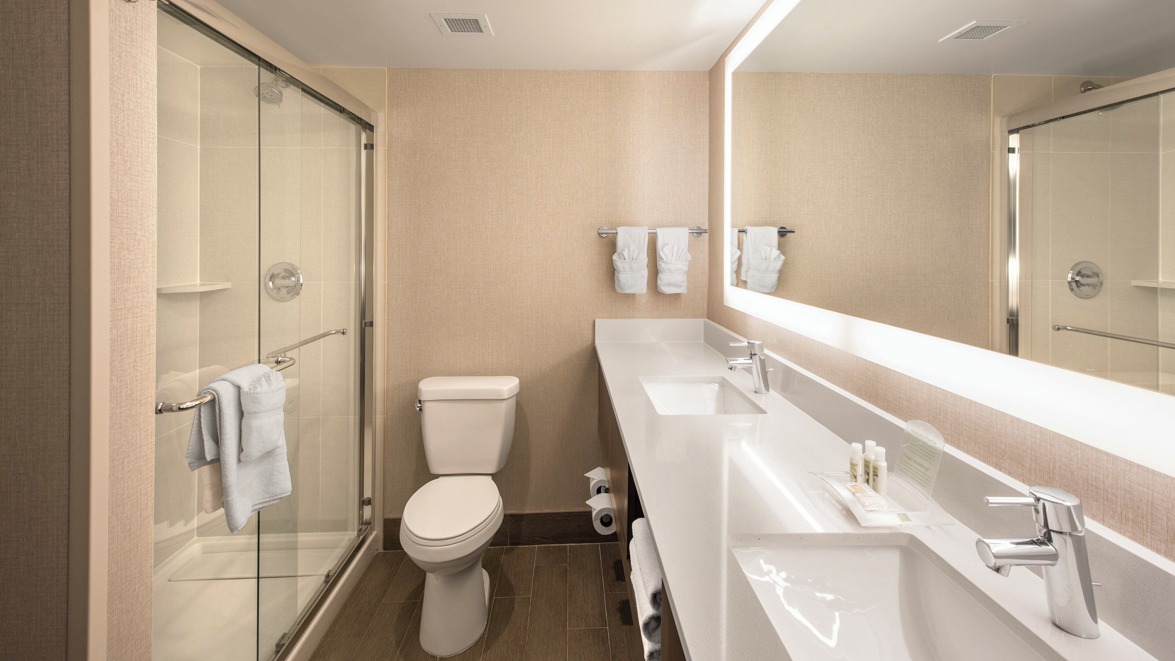 Ein modernes Badezimmer mit einer Duschkabine aus Glas, einer Toilette, einem Waschbecken mit Spiegel und einem Handtuchhalter.