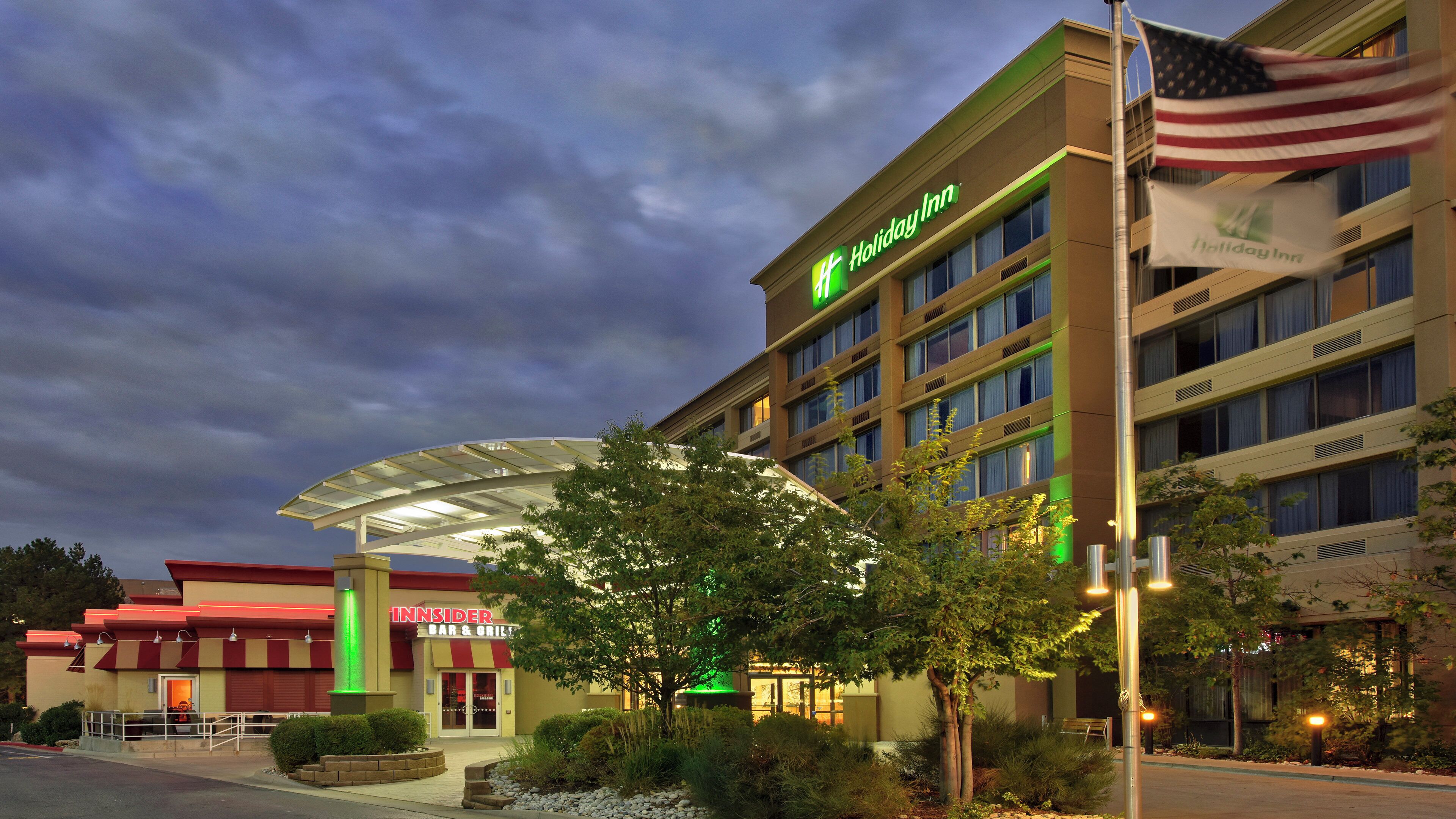 Un hotel Holiday Inn con entrada cubierta, un bar y parrilla, y una bandera estadounidense.