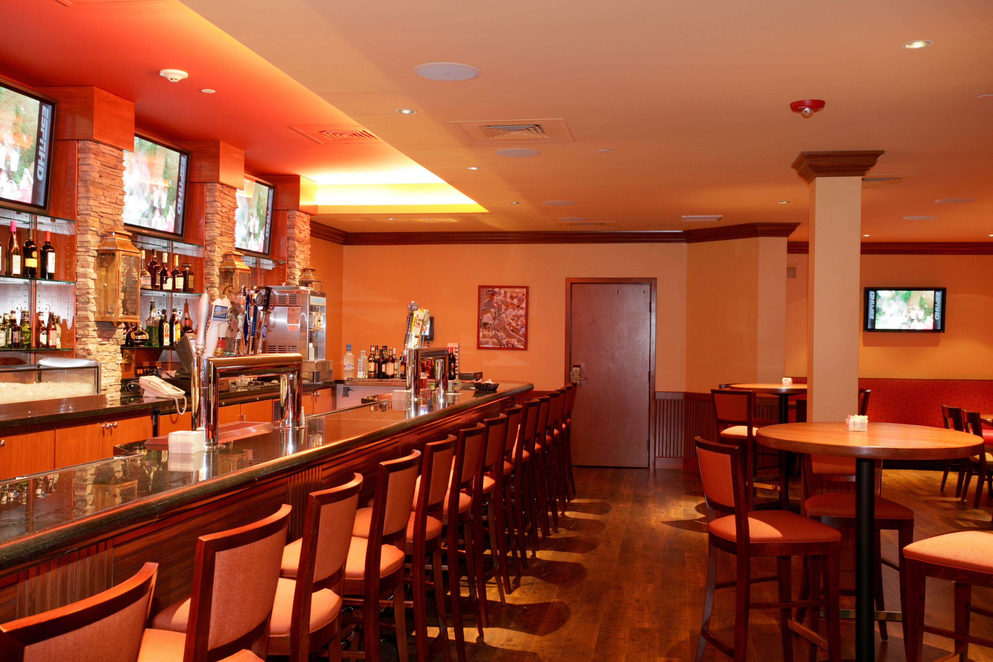 Una zona de bar con una barra larga, varios taburetes y un televisor montado en la pared.