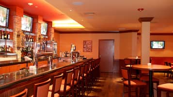 Una zona de bar con una barra larga, varios taburetes y un televisor montado en la pared.