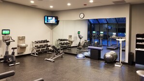 Una palestra con diverse attrezzature per esercizi, un televisore che mostra video di allenamento e un orologio appeso al muro.
