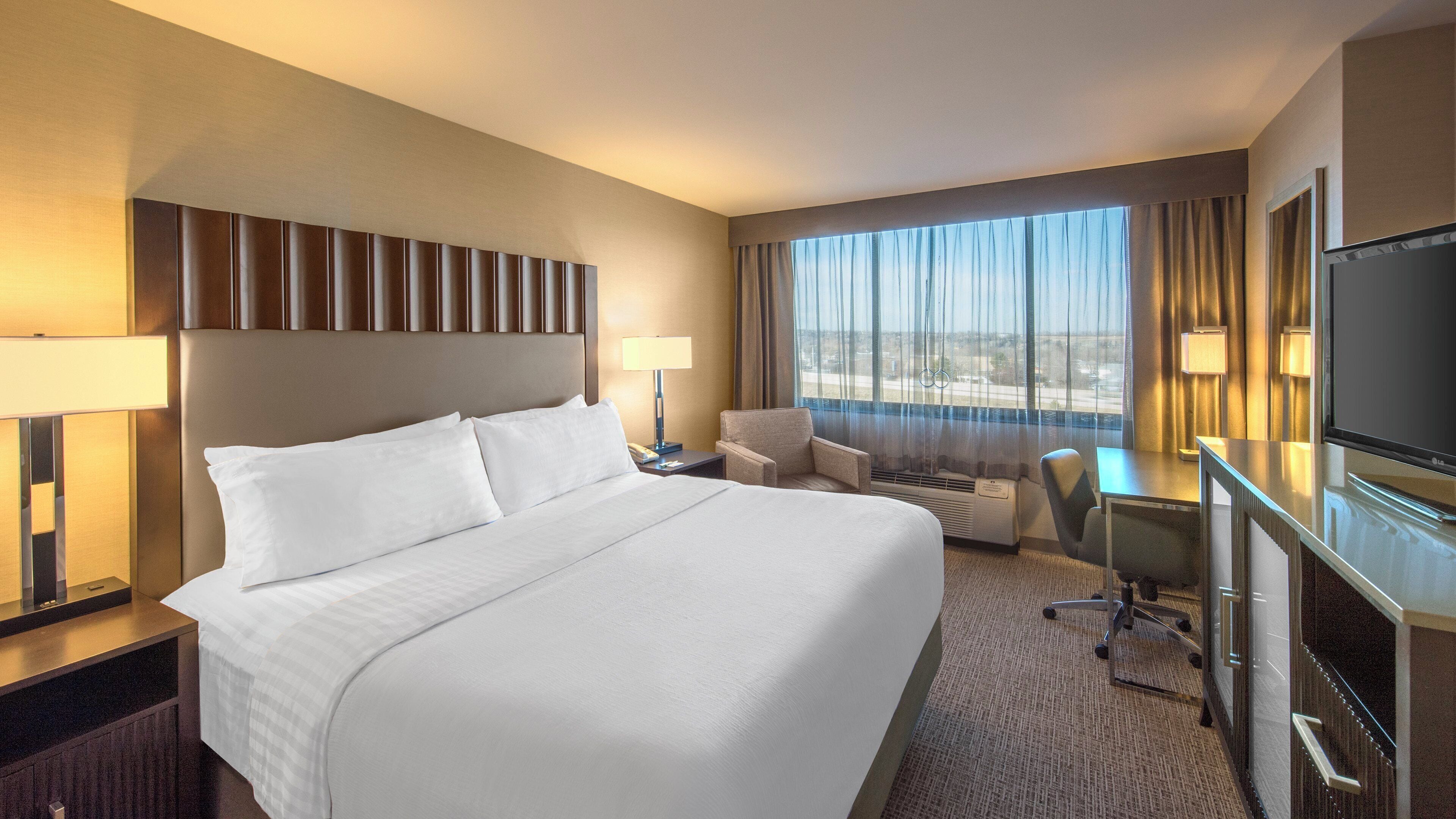 A hotel room with a large bed, a desk, a chair, a television, and a window with curtains.