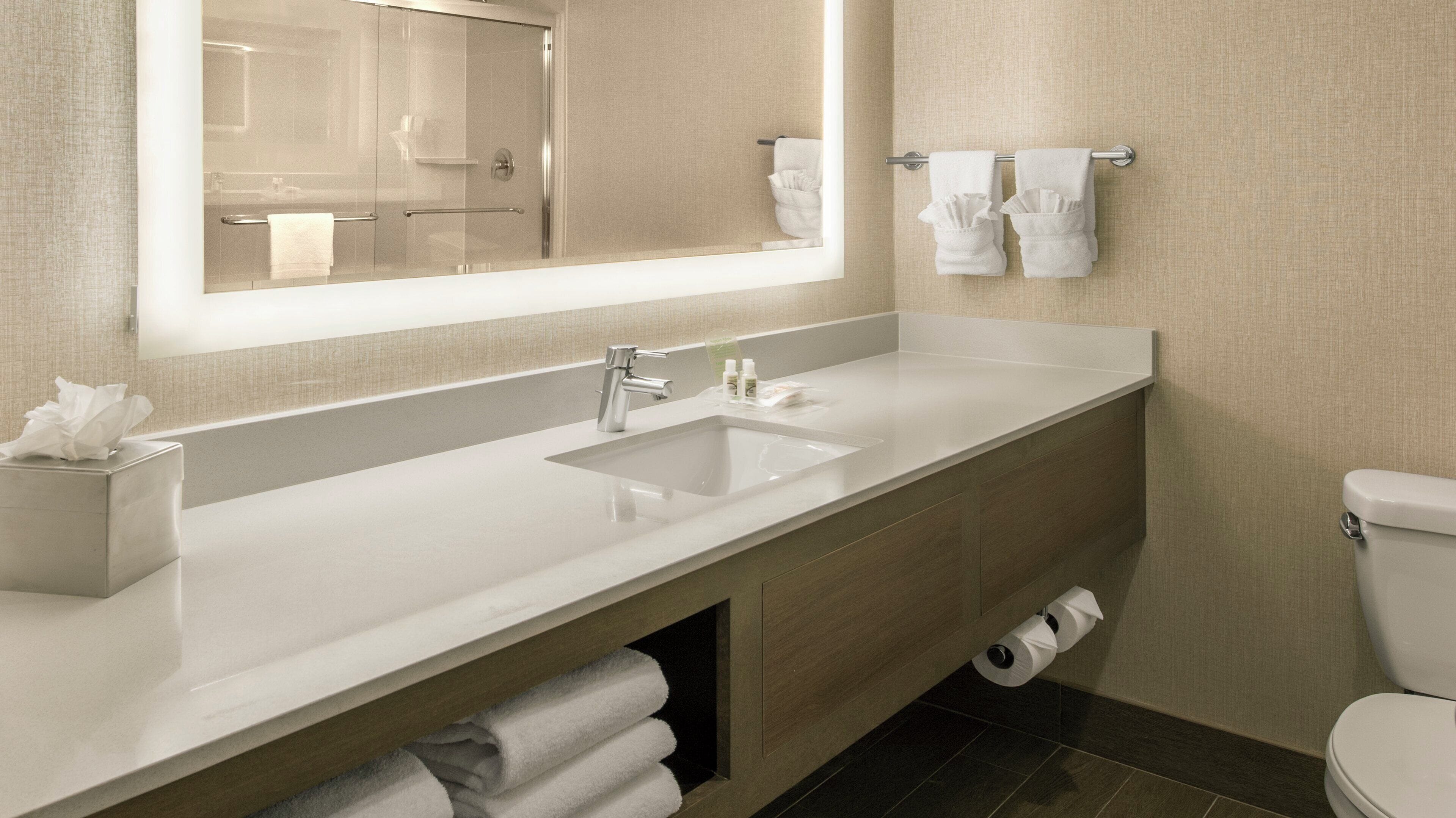 A modern bathroom with a large mirror, a sink, a toilet, and a towel rack.