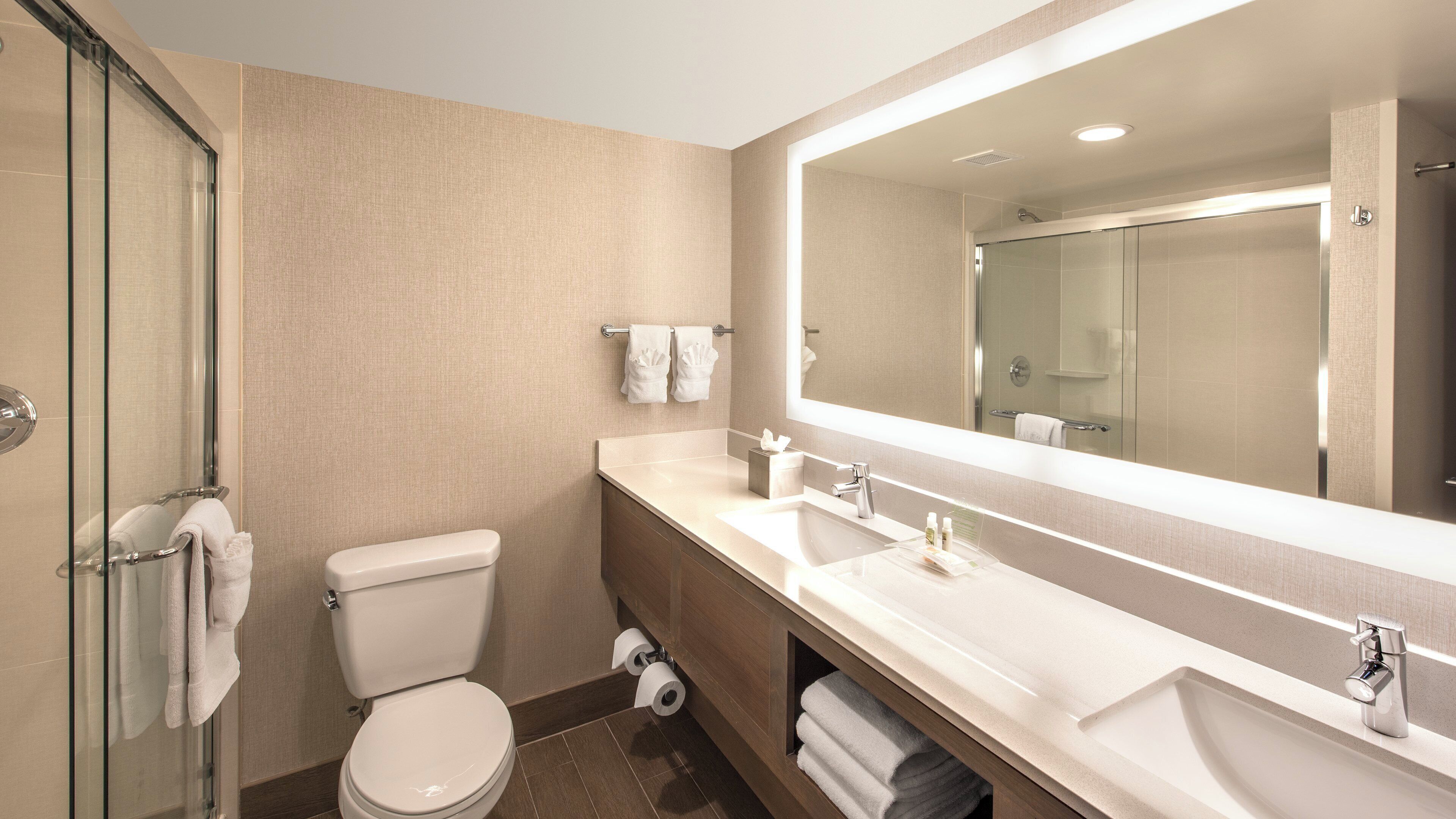 Une salle de bain moderne avec une douche à parois de verre, des toilettes, un meuble-lavabo avec un grand miroir et un évier.