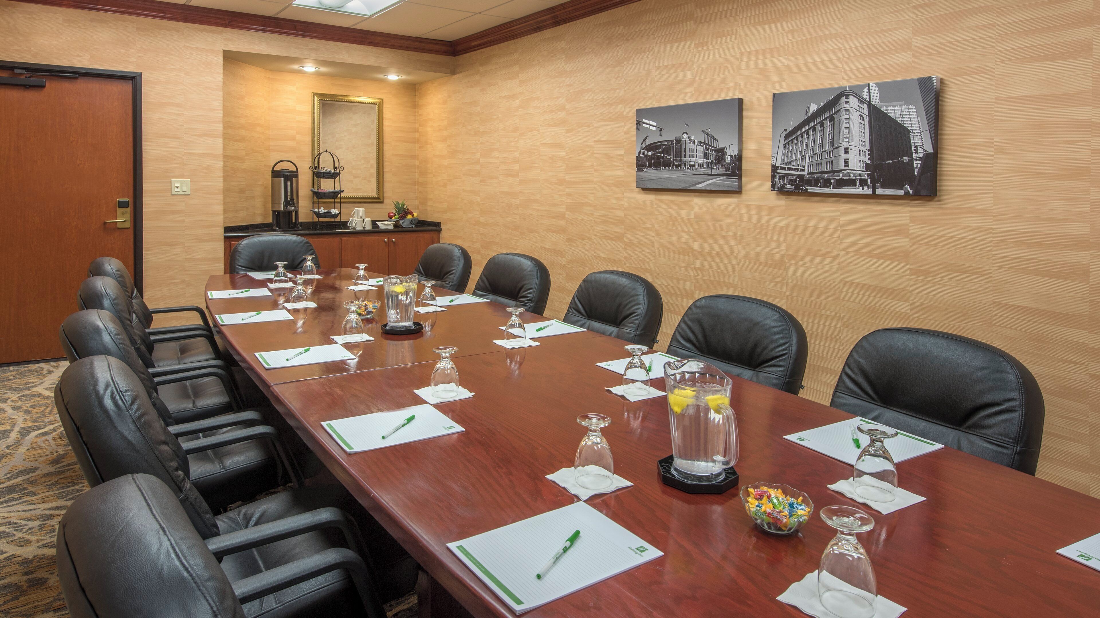 A conference room with a long table, black leather chairs, and various items like water glasses, notepads, and pens.