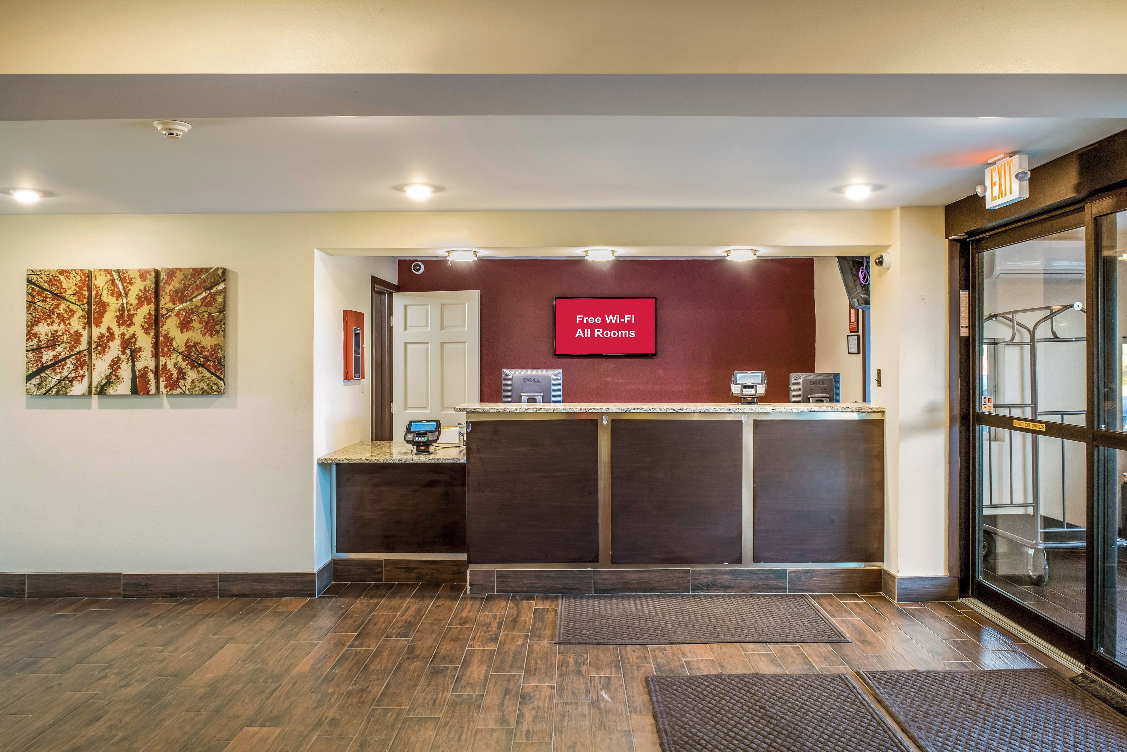 Un comptoir d’accueil doté d’un écran numérique affichant la mention « Wi-Fi gratuit dans toutes les chambres » et une caméra de surveillance placée au-dessus de la porte.
