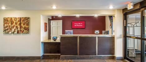 A reception desk with a digital screen displaying 'Free Wi-Fi All Rooms' and a security camera above the door.
