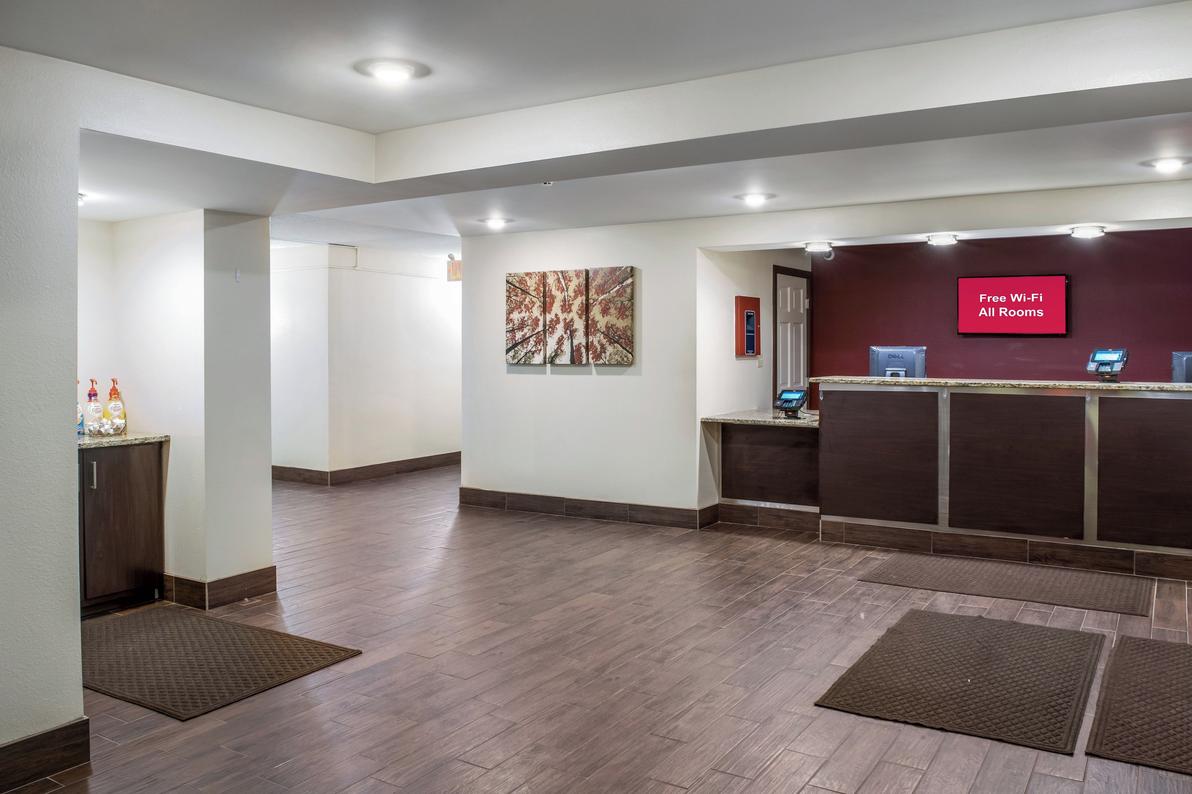 A hotel reception area with a flat-screen TV displaying 'Free Wi-Fi All Rooms' and a Dell computer.