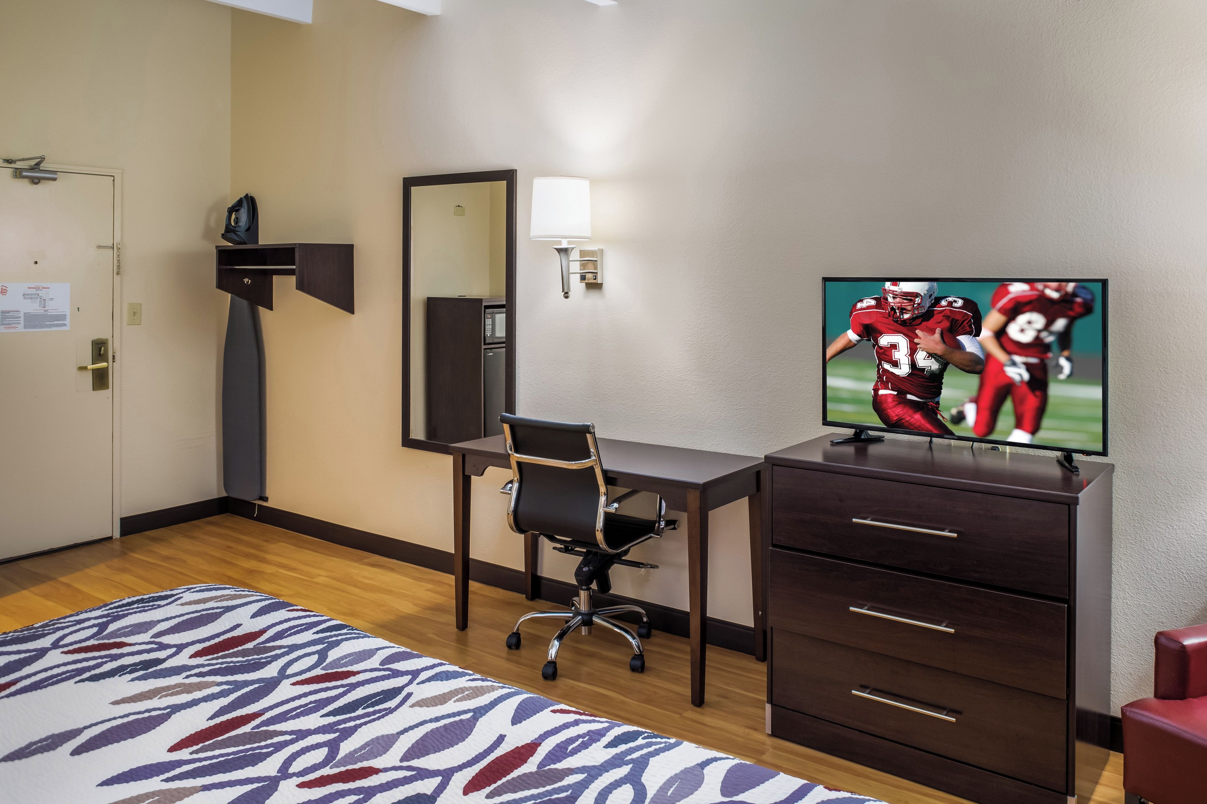 Habitación de hotel con escritorio, silla, televisor y una cama con colcha estampada.