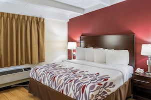 Quarto de hotel com uma cama grande, uma mesa de cabeceira com abajur e telefone fixado na parede.