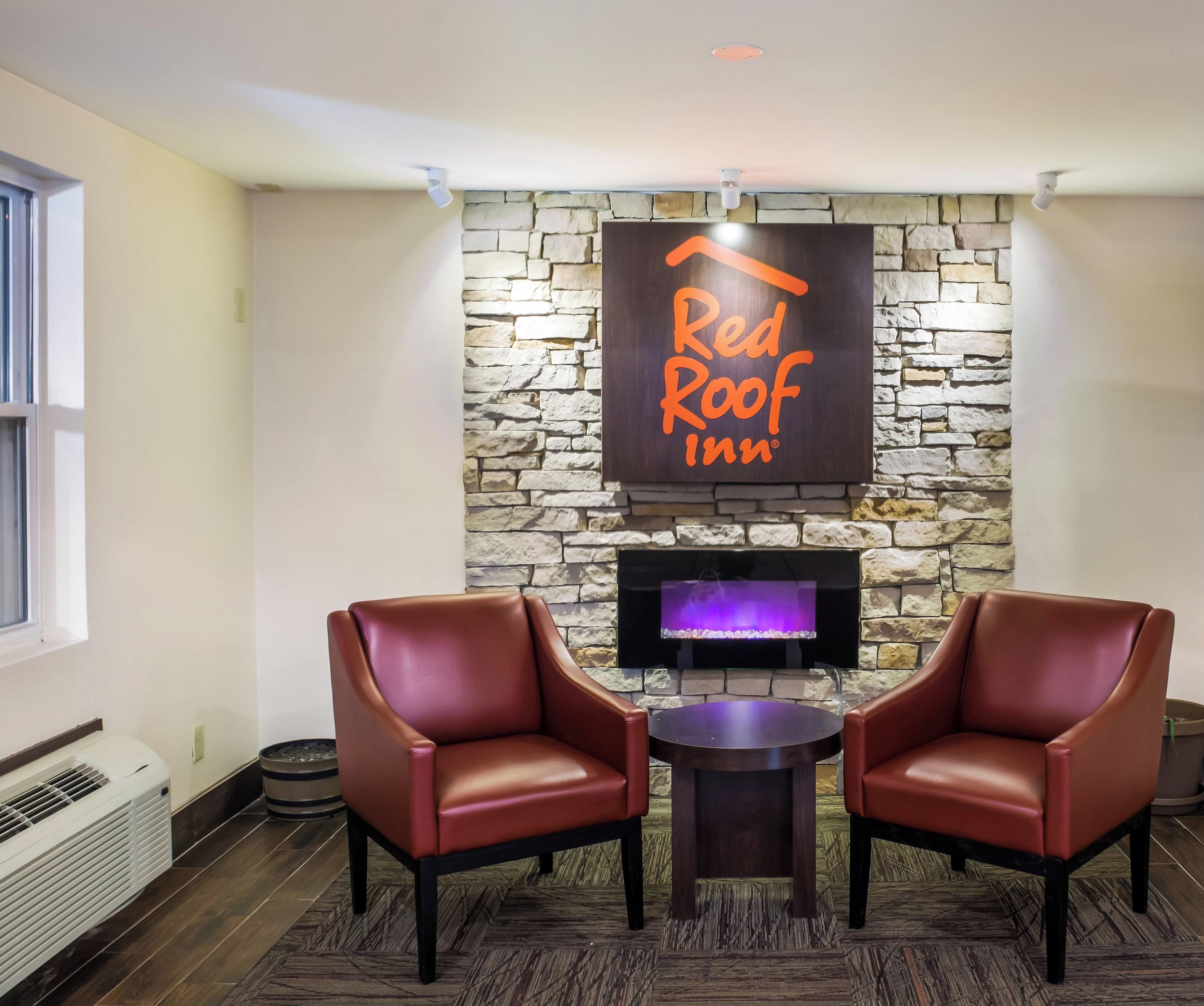 Un hall d’entrée de Red Roof Inn avec des murs en pierre, une cheminée, des fauteuils en cuir et un téléviseur à écran plat.