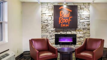 Un hall d’entrée de Red Roof Inn avec des murs en pierre, une cheminée, des fauteuils en cuir et un téléviseur à écran plat.
