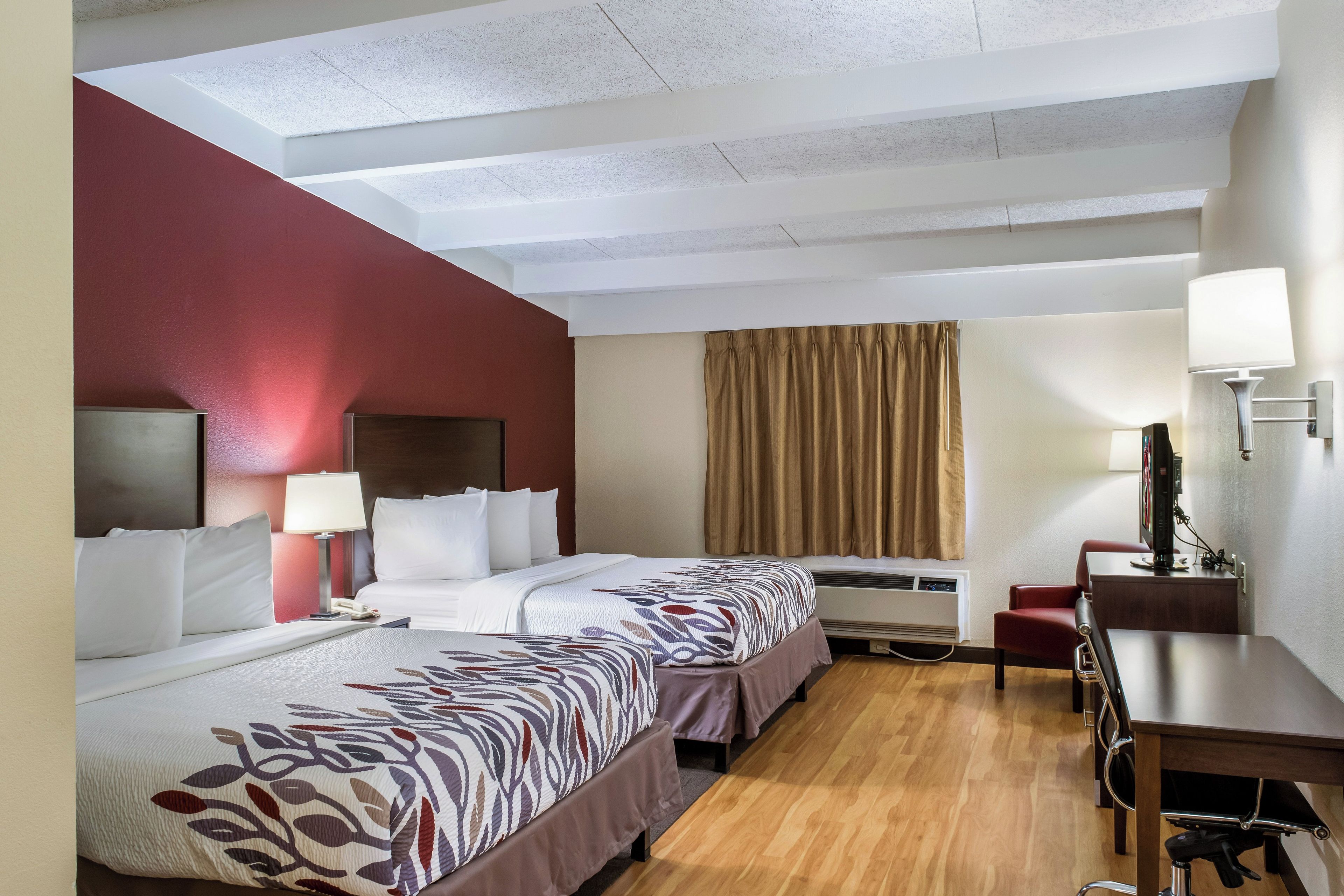 Una habitación de hotel con dos camas, un escritorio, una silla, un televisor y un aire acondicionado.