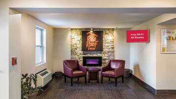A Red Roof Inn lobby with a stone fireplace, two leather chairs, a fire feature, and a sign indicating free Wi-Fi in all rooms.
