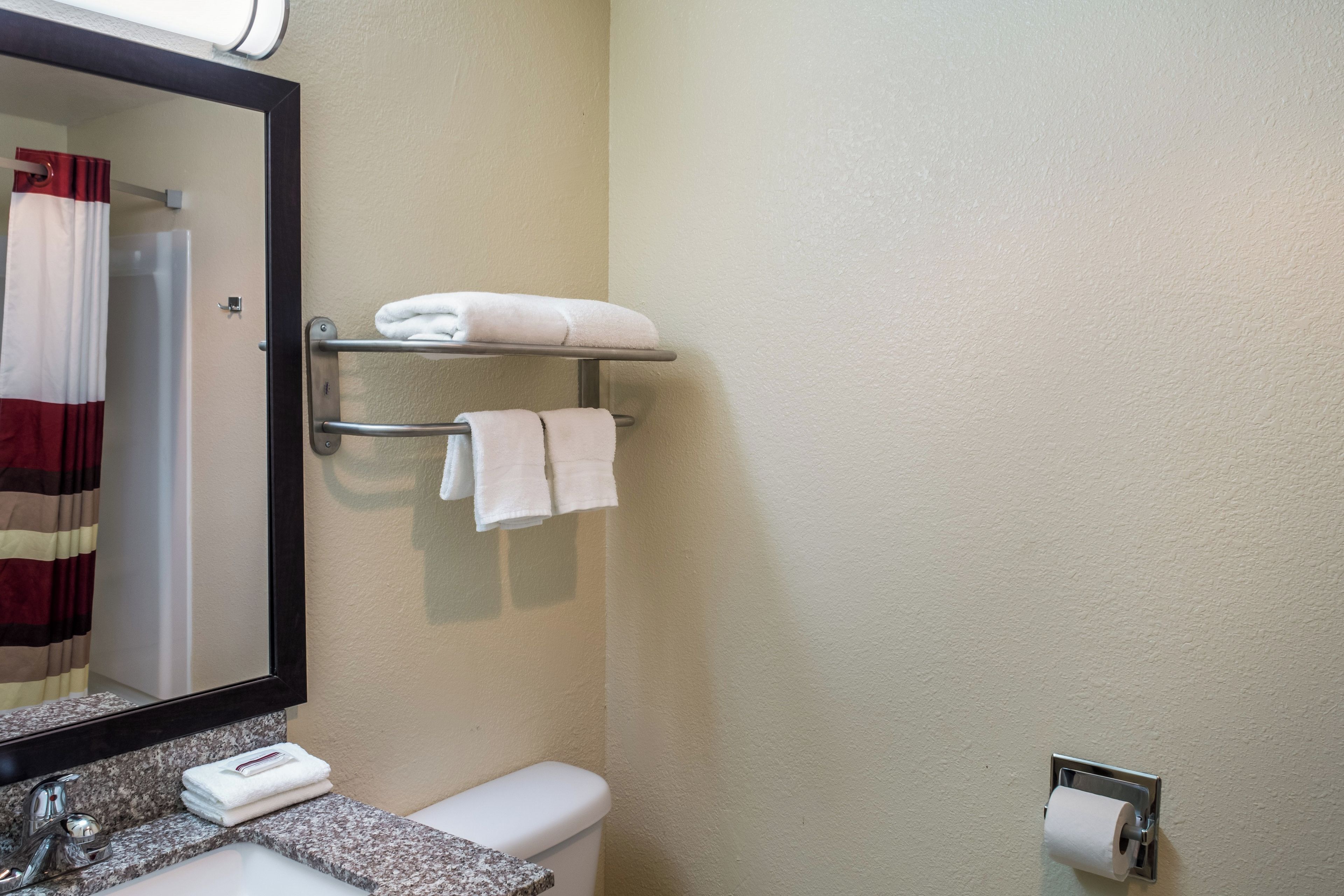 A bathroom with a toilet, a sink, a towel rack with folded towels, a mirror, and a shower curtain.