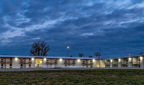 A motel with multiple rooms, a fenced parking area, and a grassy foreground. - Red Roof Inn Richmond, IN (Richmond)