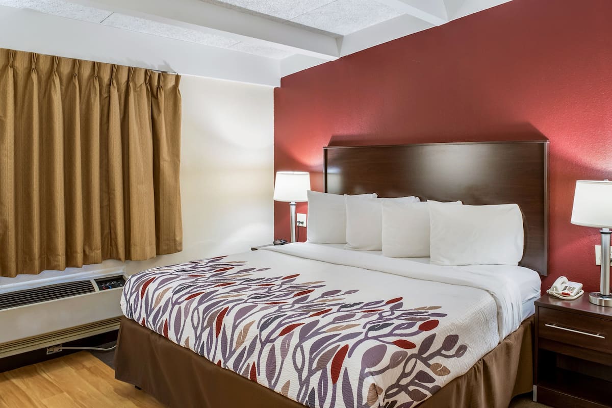 A hotel room with a large bed, a bedside table with a lamp, and a wall-mounted phone.
