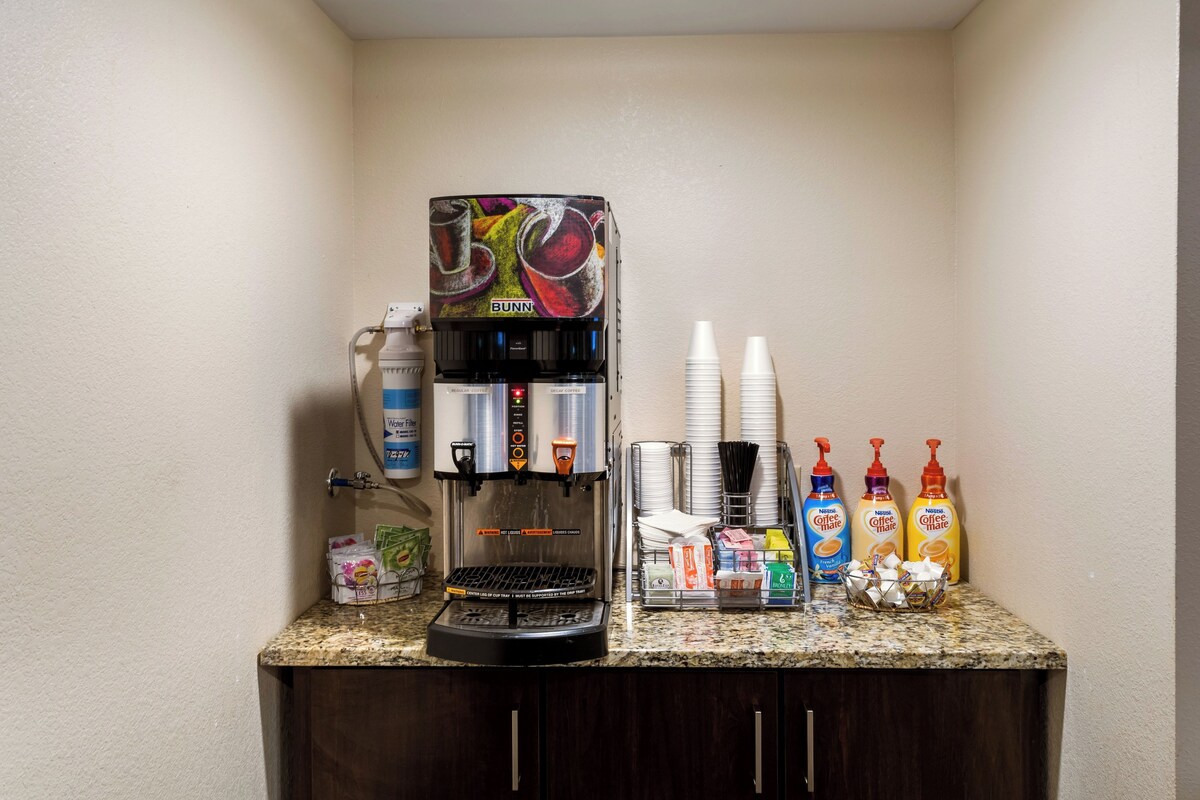A coffee station with a coffee machine, disposable cups, and coffee creamer bottles.