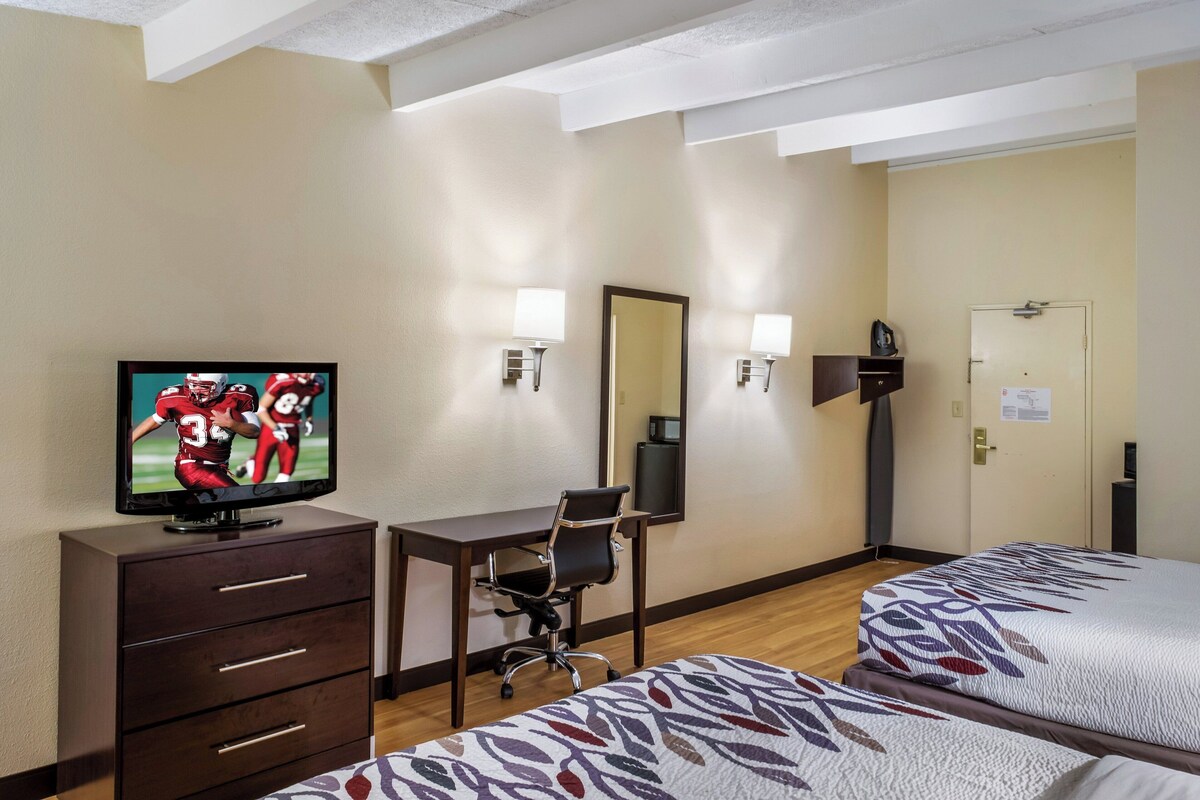 A hotel room with a TV on a dresser, a desk with a chair, two beds, and a door.