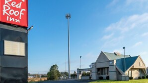 A Red Roof Inn with a clear sky, a tall communication tower, and a building with a blue roof. - Red Roof Inn Richmond, IN (Richmond)