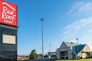 A Red Roof Inn with a clear sky, a tall communication tower, and a building with a blue roof. - Red Roof Inn Richmond, IN (Richmond)