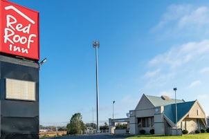 Un hotel Red Roof Inn con cielo despejado, una alta torre de comunicaciones y un edificio con techo azul.