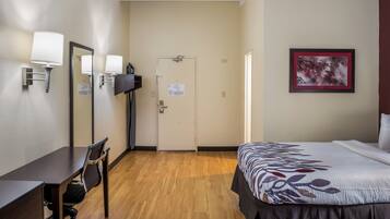 A hotel room with a bed, a desk with a chair, a television, and a door.
