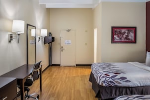 Quarto de hotel com cama, escrivaninha com cadeira, televisão e porta.