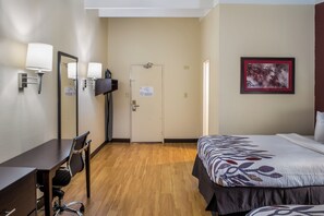 Una habitación de hotel con una cama, un escritorio con una silla, un televisor y una puerta.