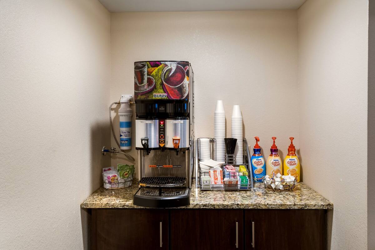 A coffee station with a Bunn coffee machine, disposable cups, and coffee creamer bottles.