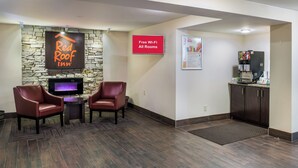 A Red Roof Inn lobby with a stone wall, two leather chairs, a flat-screen TV, a Red Roof Plus sign, and a Red Roof coffee machine. - Red Roof Inn Richmond, IN (Richmond)