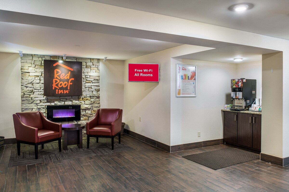 A Red Roof Inn lobby with a stone fireplace, leather chairs, a flat-screen TV, and a sign indicating free Wi-Fi in all rooms.