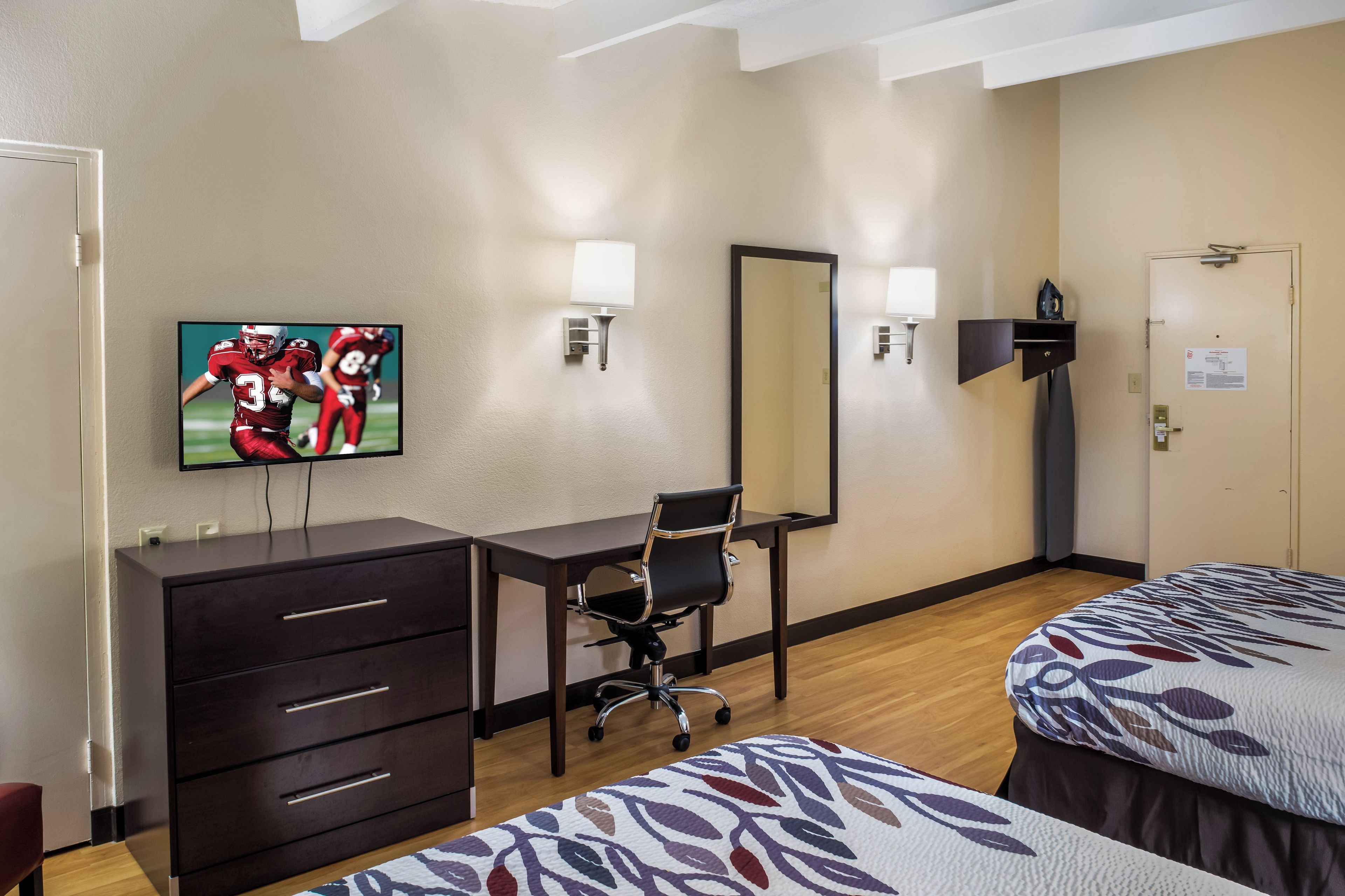 A hotel room with a TV, desk, chair, and two beds.