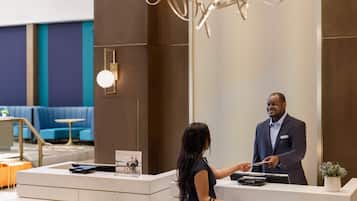A reception desk with a man and a woman interacting, a modern interior with blue seating, and a decorative wall.