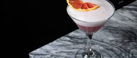 Un verre à martini contenant une boisson mousseuse et décoré d’une tranche d’orange séchée, le tout posé sur une surface en marbre.