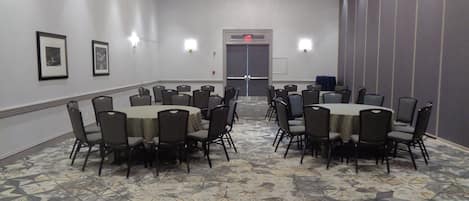 Un salón de conferencias con mesas y sillas redondas, una alfombra estampada y una araña.