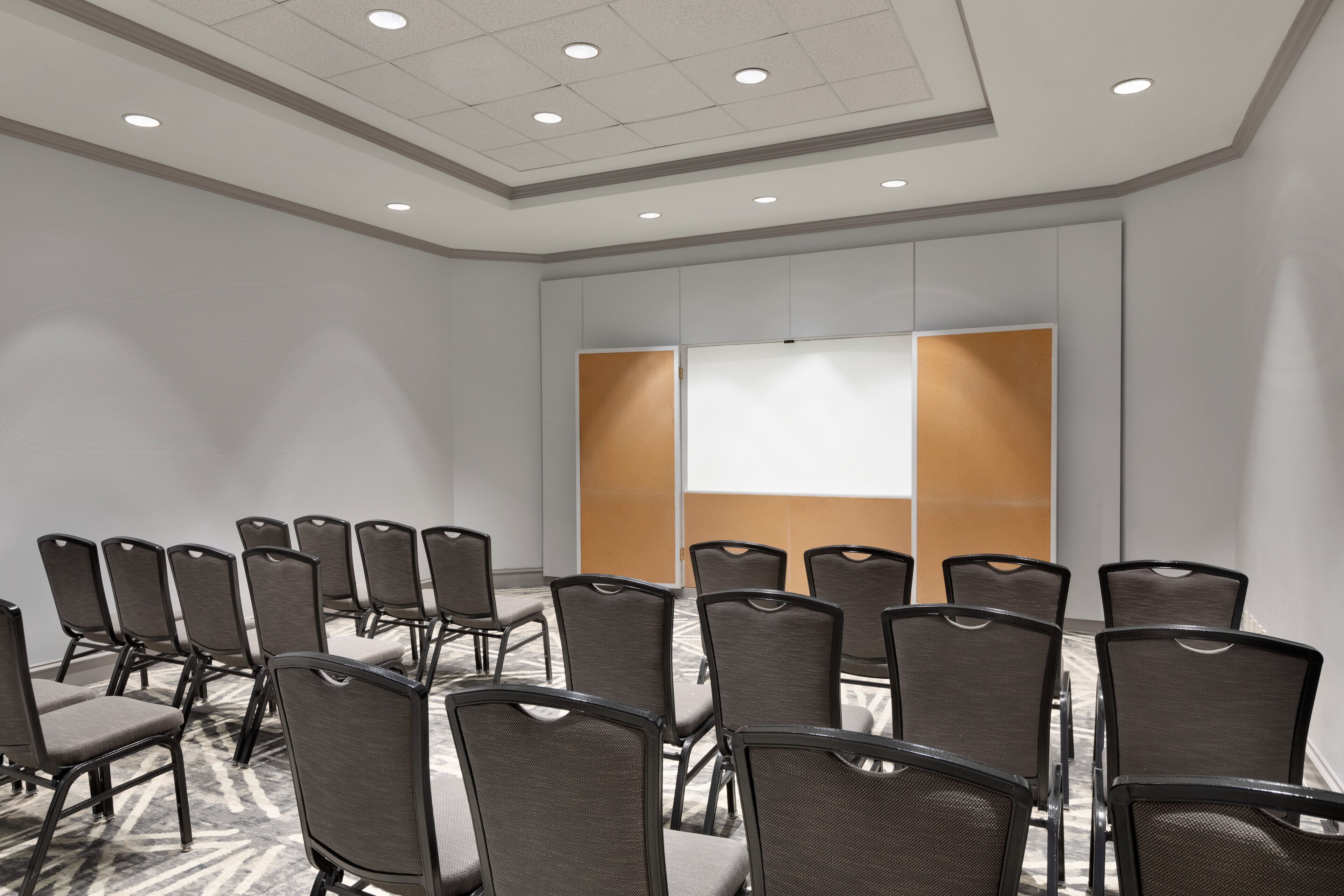 Un salón de conferencias con filas de sillas, una pantalla grande y una decoración en colores neutros.