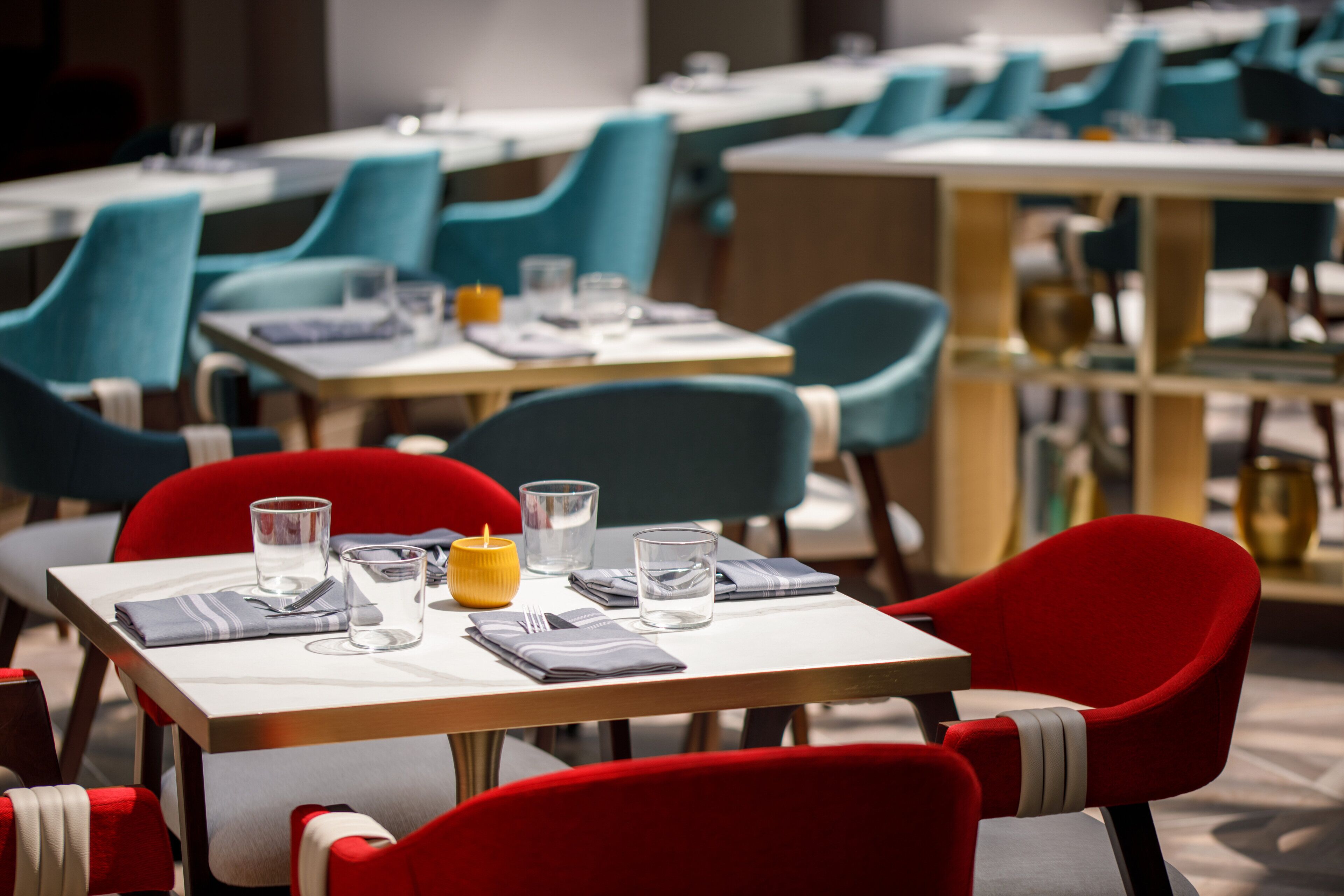 Een restaurant met gedekte tafels, met teal- en rode stoelen.