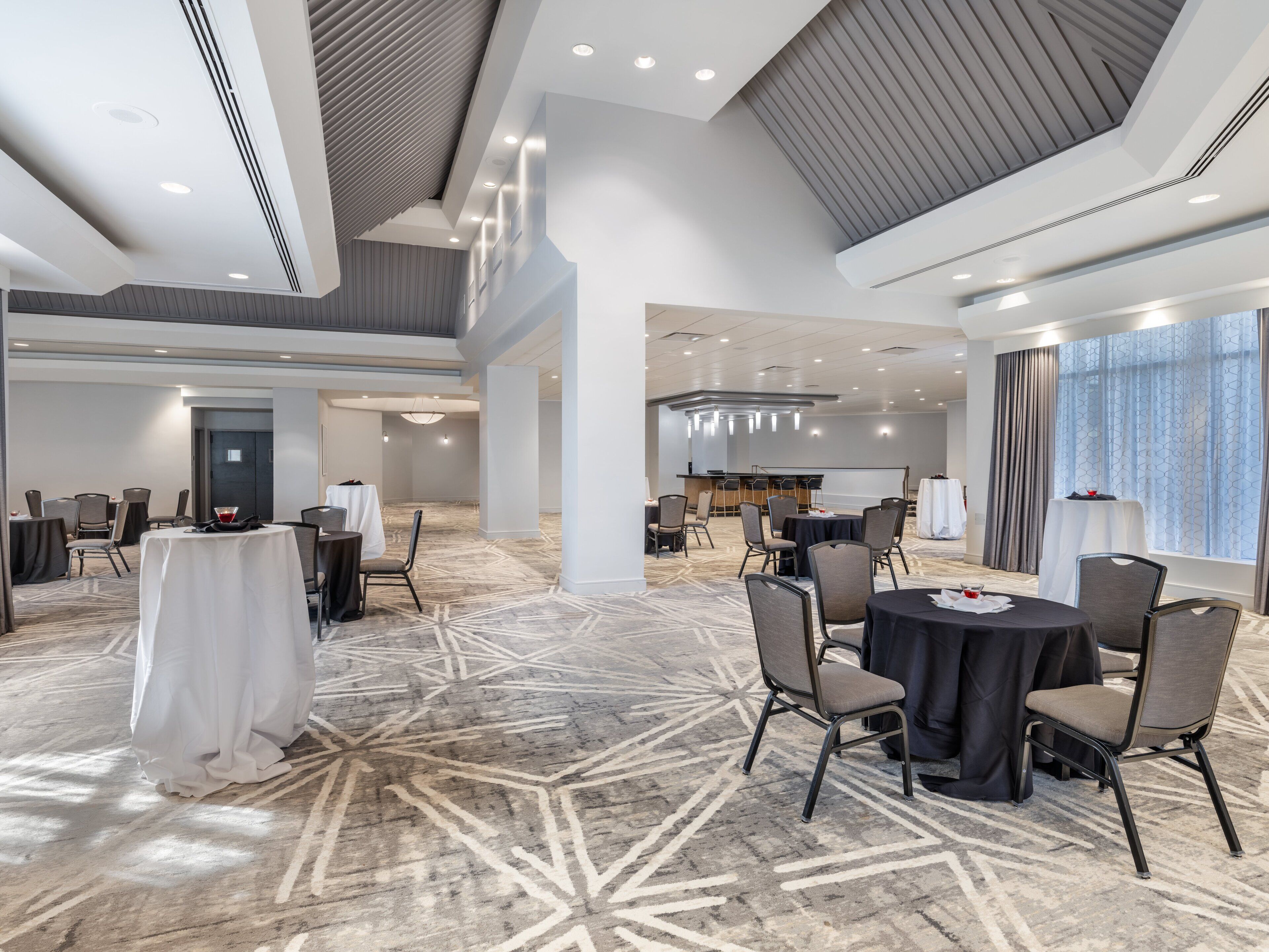 Una sala de conferencias amplia con techos altos, iluminación moderna y alfombra estampada.