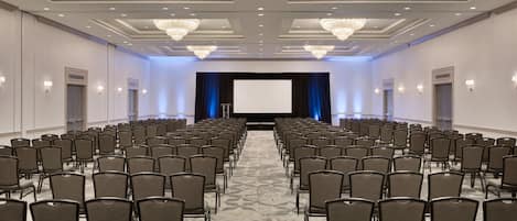 A conference room with rows of chairs, a large screen, and chandeliers.