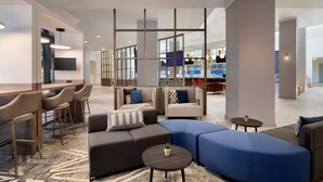 A modern hotel lobby with a bar area, seating arrangements, and a large window providing a view of the city.