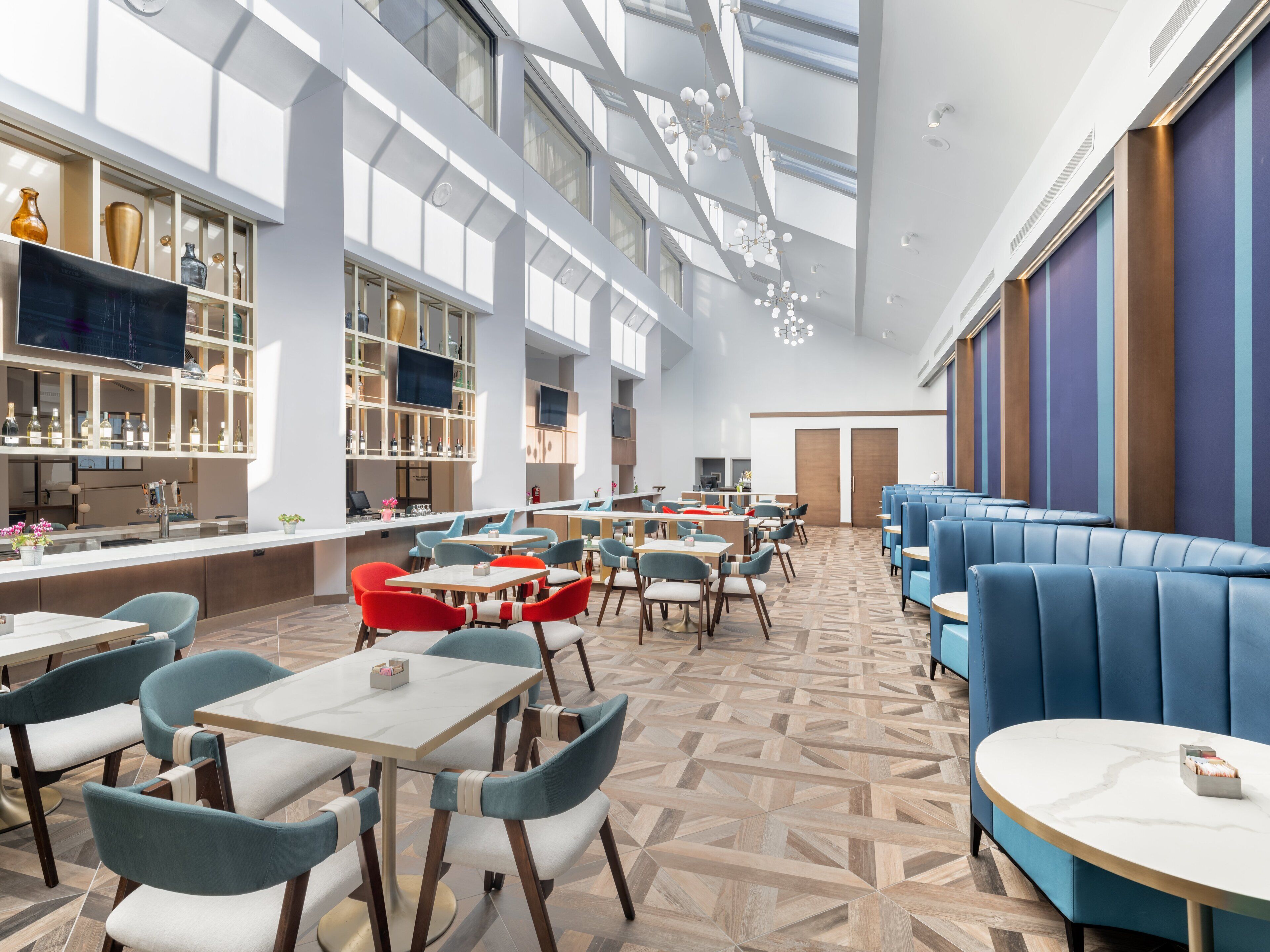 A modern restaurant with high ceilings, large windows, and a variety of seating options including tables and booths.