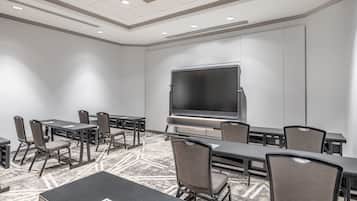 A conference room with a large flat-screen TV, multiple tables and chairs, and a carpeted floor.