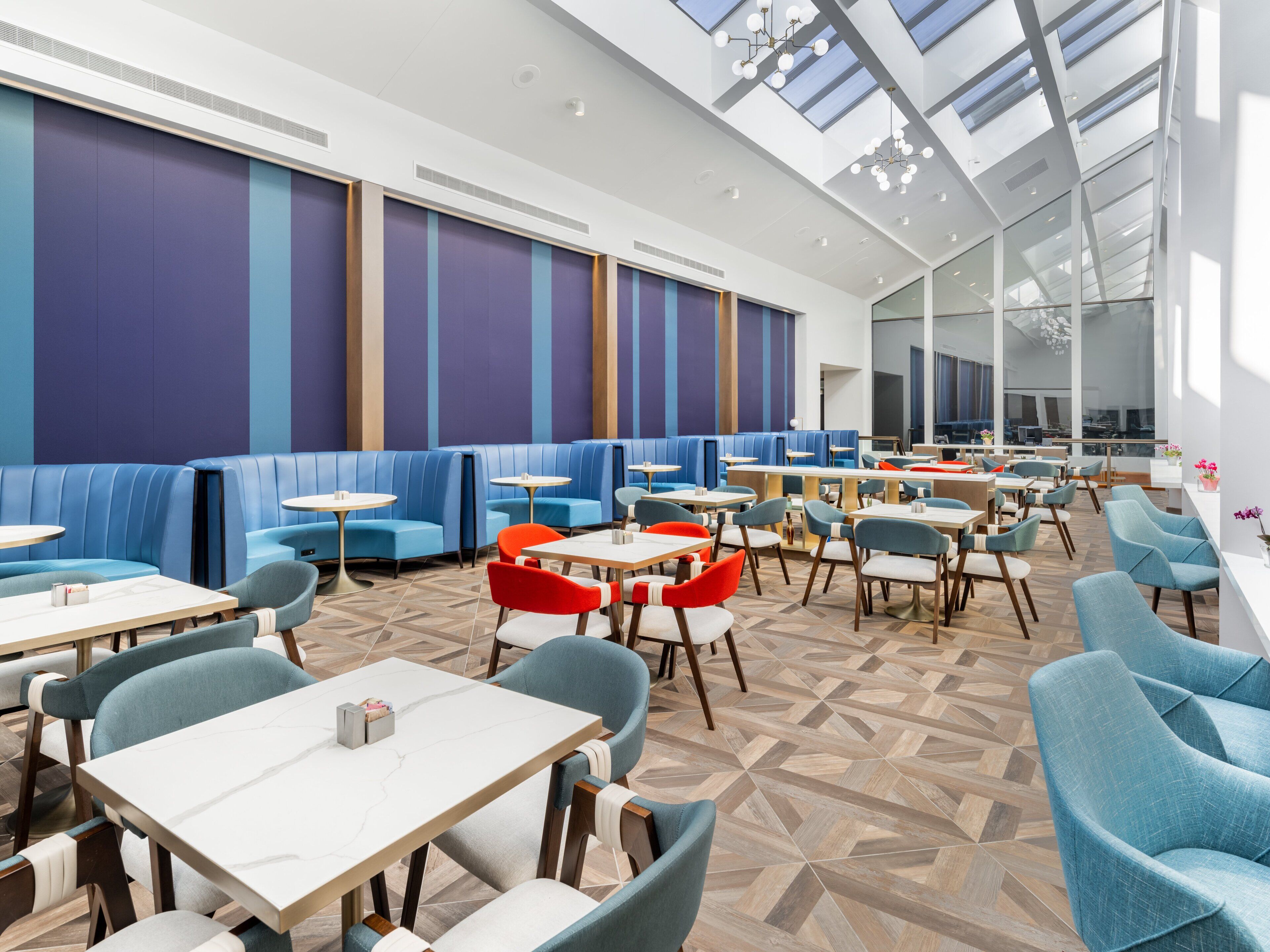 A modern restaurant with blue booths, round tables, and a high ceiling with skylights.