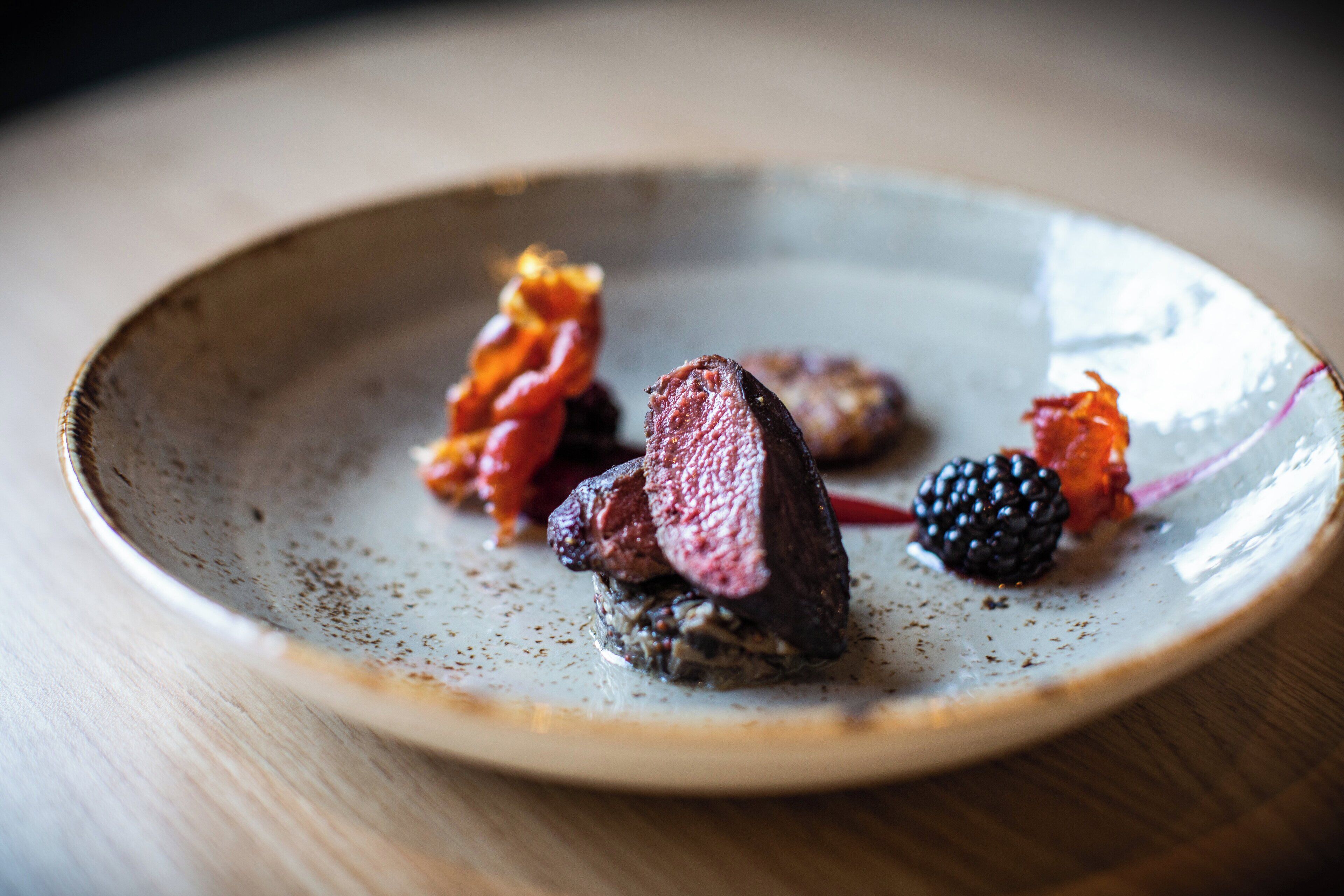 A plate with a piece of meat, some berries, and a leaf.
