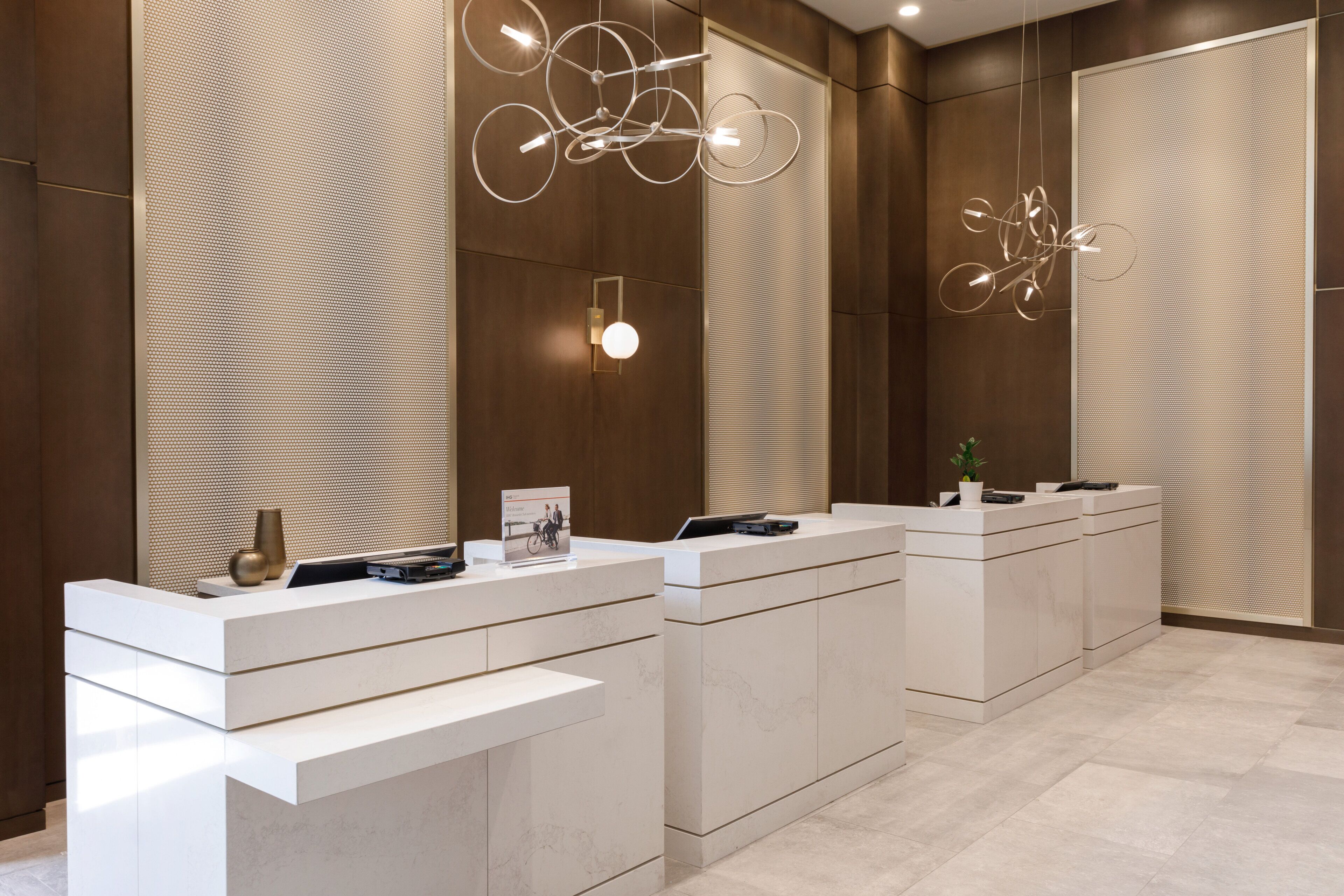A modern reception area with three white reception desks, a large mirror, and contemporary pendant lighting.