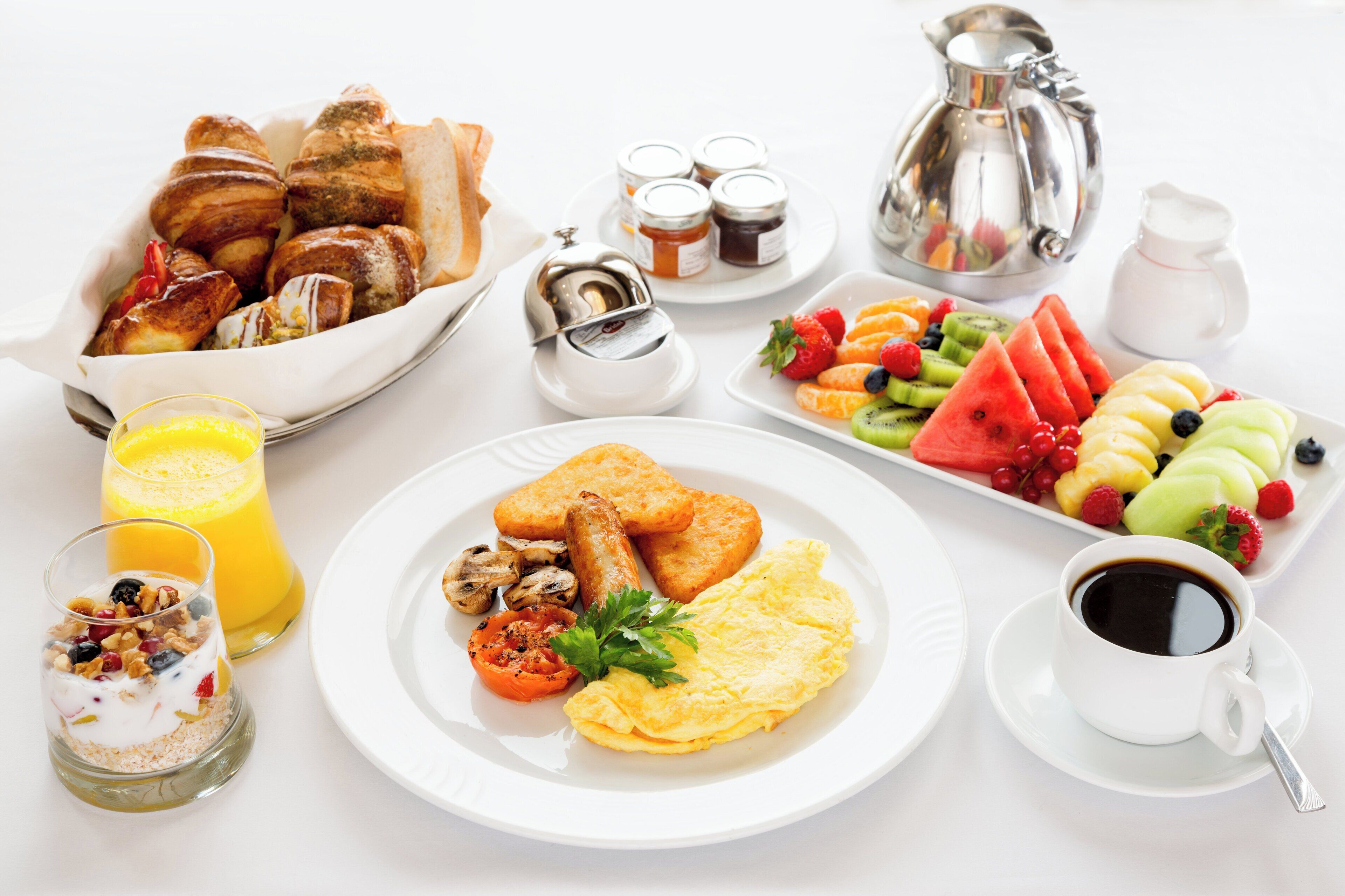 A breakfast table with croissants, toast, eggs, fruits, and beverages.