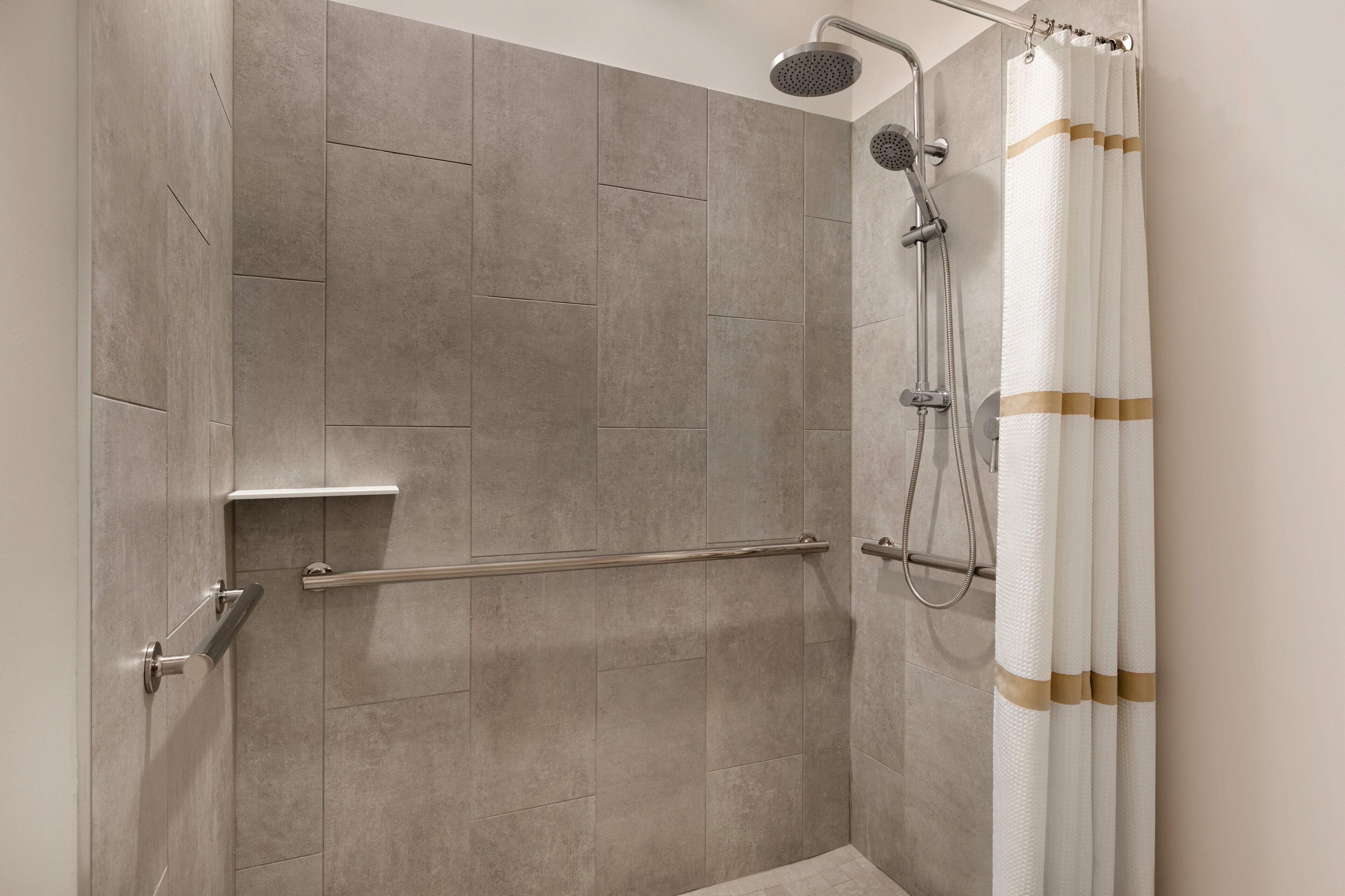 A shower area with a glass door, a handrail, and a showerhead.